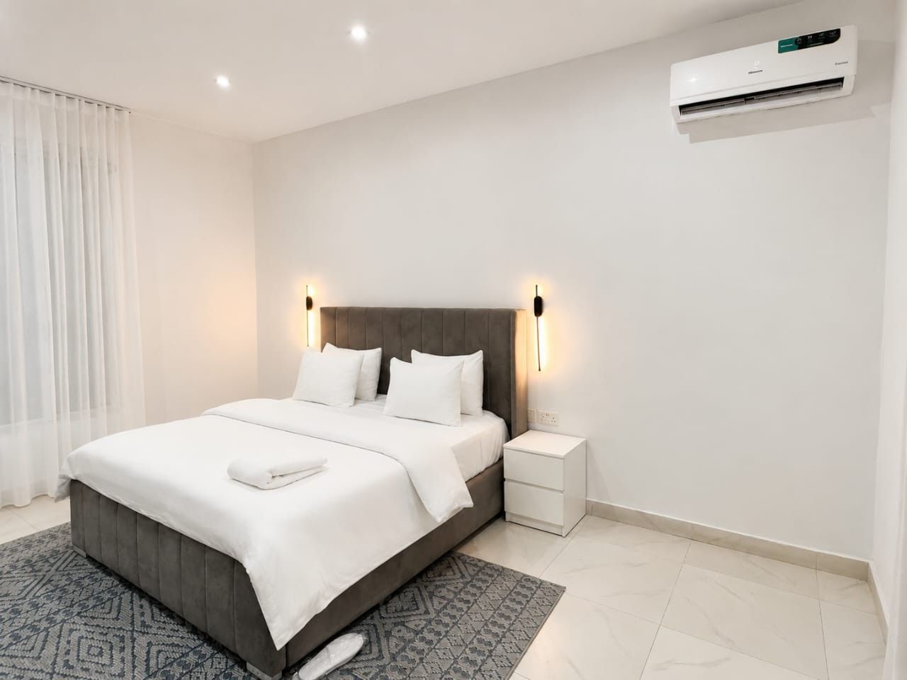 Une chambre moderne comprenant un lit, des tables de chevet, un tapis et un appareil de climatisation.