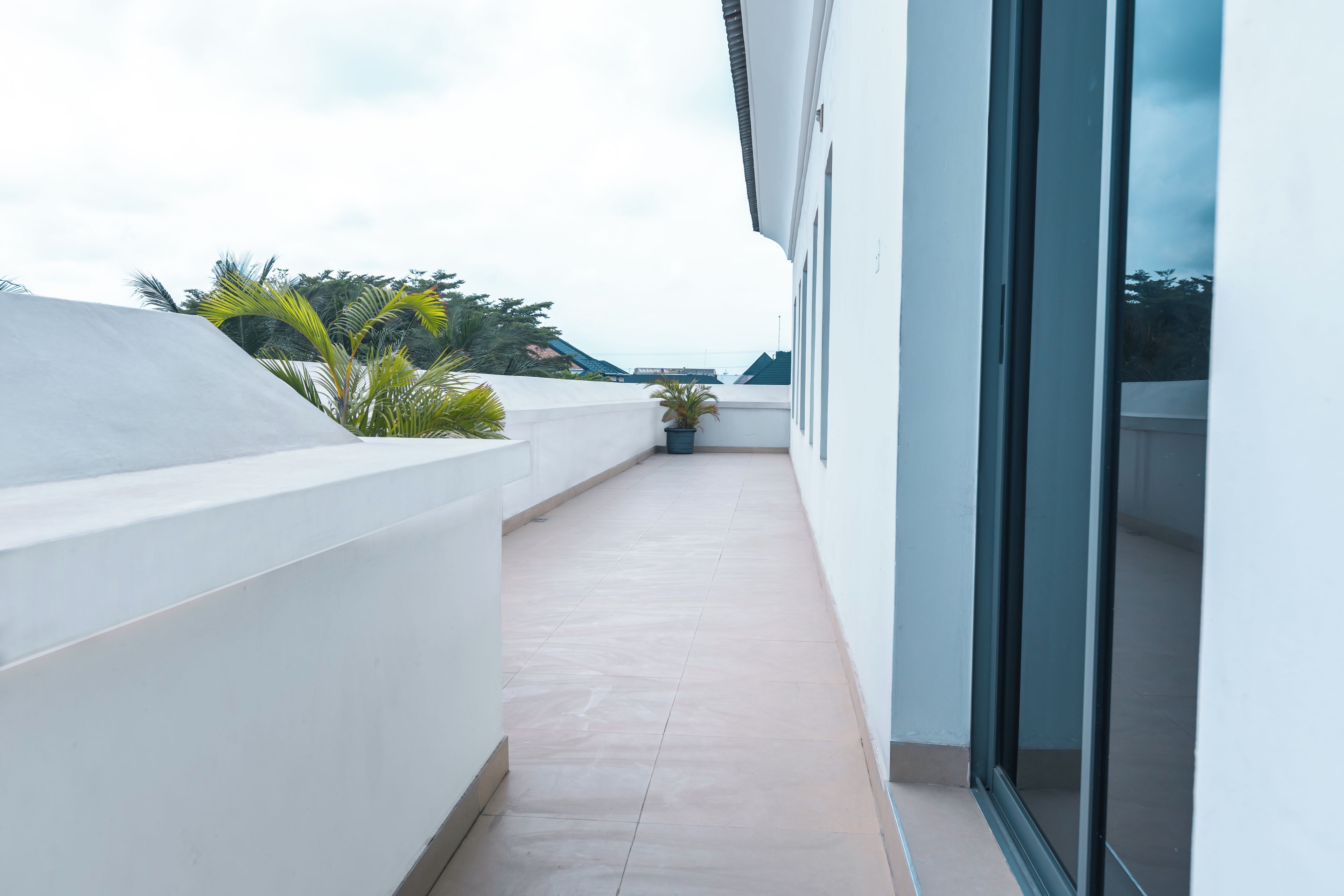 A narrow balcony with a tiled floor, white walls, and a potted plant.