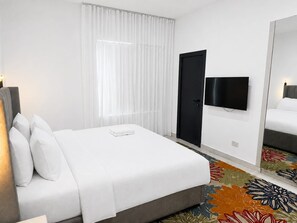 A hotel room with a bed, a television, a door, and a mirror. - Bluerock Residences (Lekki)
