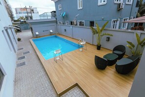 A rooftop swimming pool with a wooden deck, a few chairs, and potted plants. - Bluerock Residences (Lekki)