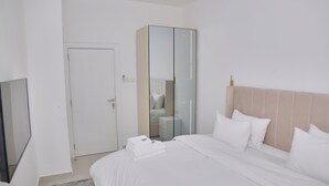 Et hotelværelse med seng, garderobeskab, spejl og fjernsyn.
