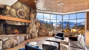 Un intérieur moderne agrémenté d’une cheminée en pierre, de grandes fenêtres offrant une vue sur les montagnes et de meubles contemporains.