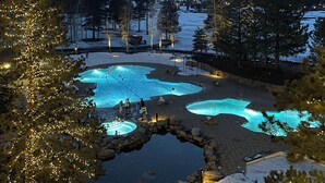 Un paysage enneigé avec un espace piscine illuminé par des jeux de lumière, entouré d’arbres et de montagnes.