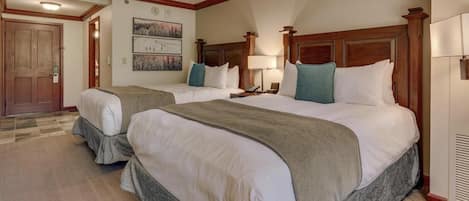 A hotel room with two beds, a wooden headboard, a nightstand, a lamp, and a door.