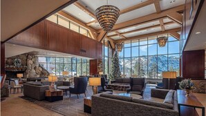 Un hall d’entrée spacieux avec une cheminée en pierre, de grandes fenêtres offrant une vue sur les montagnes et un mobilier moderne.