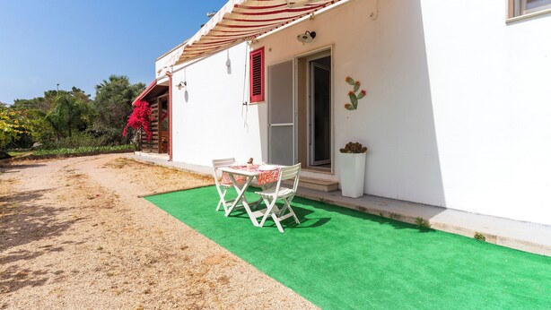 A white building with a red and white striped awning, a green artificial lawn, and a table with chairs outside.