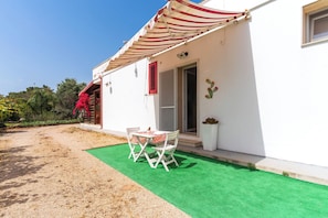 A white building with a red and white striped awning, a green artificial lawn, and a table with chairs outside. - 3977 Appartamento di Stefy by Barbarhouse (Porto Cesareo)