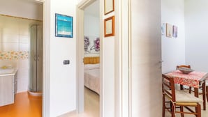 A hotel room with a bathroom, a dining area with a table and chairs, and a bed with a floral headboard.