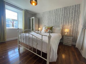 Een slaapkamer met een bed met wit metalen frame, een nachtkastje met lamp en een kledingkast.