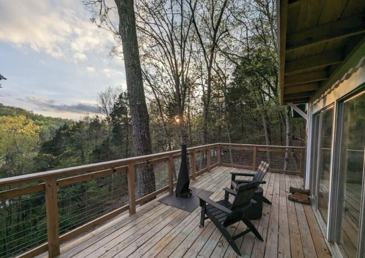 Une terrasse en bois avec des sièges d’extérieur et un barbecue, donnant sur une zone boisée.