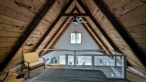 Une chambre mansardée avec un plafond en pente, un lit, une chaise, un bureau et une fenêtre.