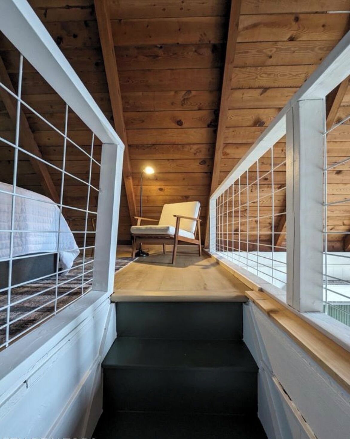 Una stretta scala conduce a una camera da letto soppalcata con un letto e una poltrona.