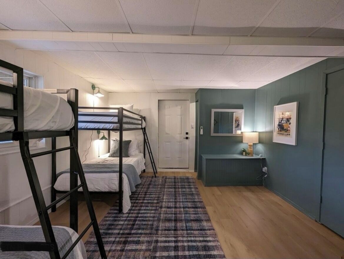 Une chambre de type dortoir, avec des lits superposés, un bureau, une chaise, une lampe et une porte.