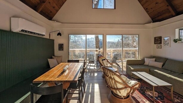 Une pièce spacieuse avec un plafond haut, de grandes fenêtres, une table à manger en bois et un canapé.