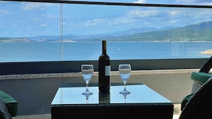Una mesa con una botella y dos vasos, con vista a un paisaje marino y colinas lejanas.