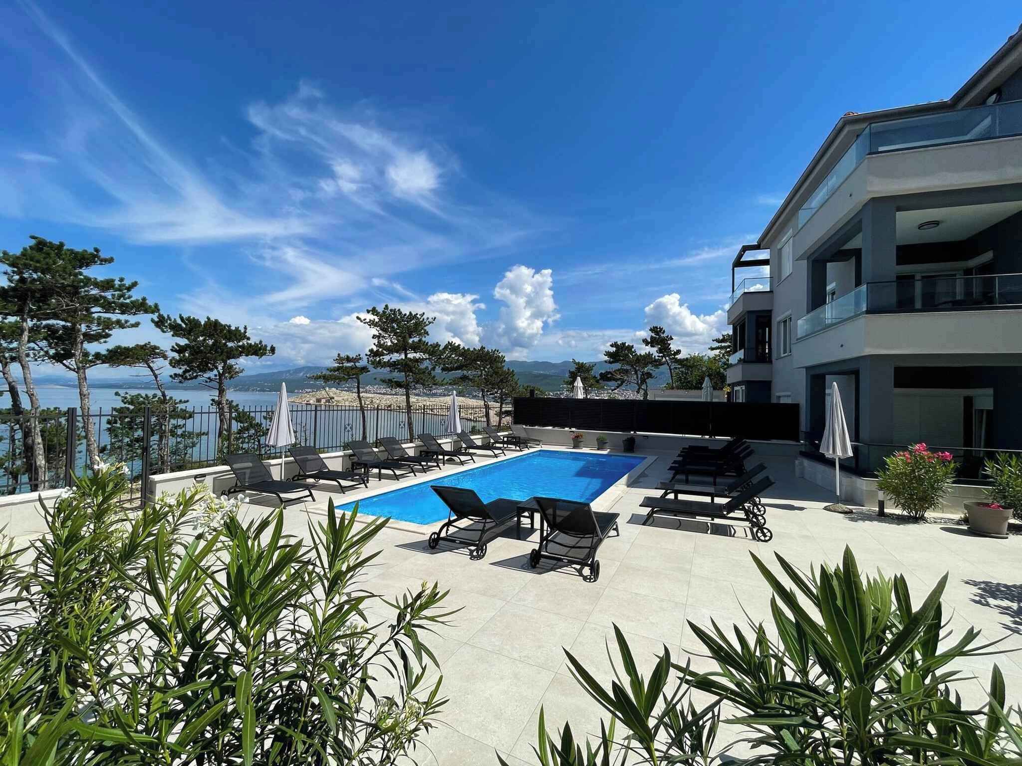 A rooftop pool area with lounge chairs, a pool table, and a view of the sea.