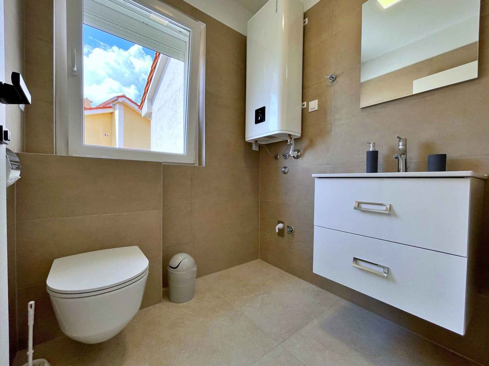 Une salle de bain avec des toilettes, un lavabo avec un miroir et une fenêtre donnant sur un bâtiment à l’extérieur.