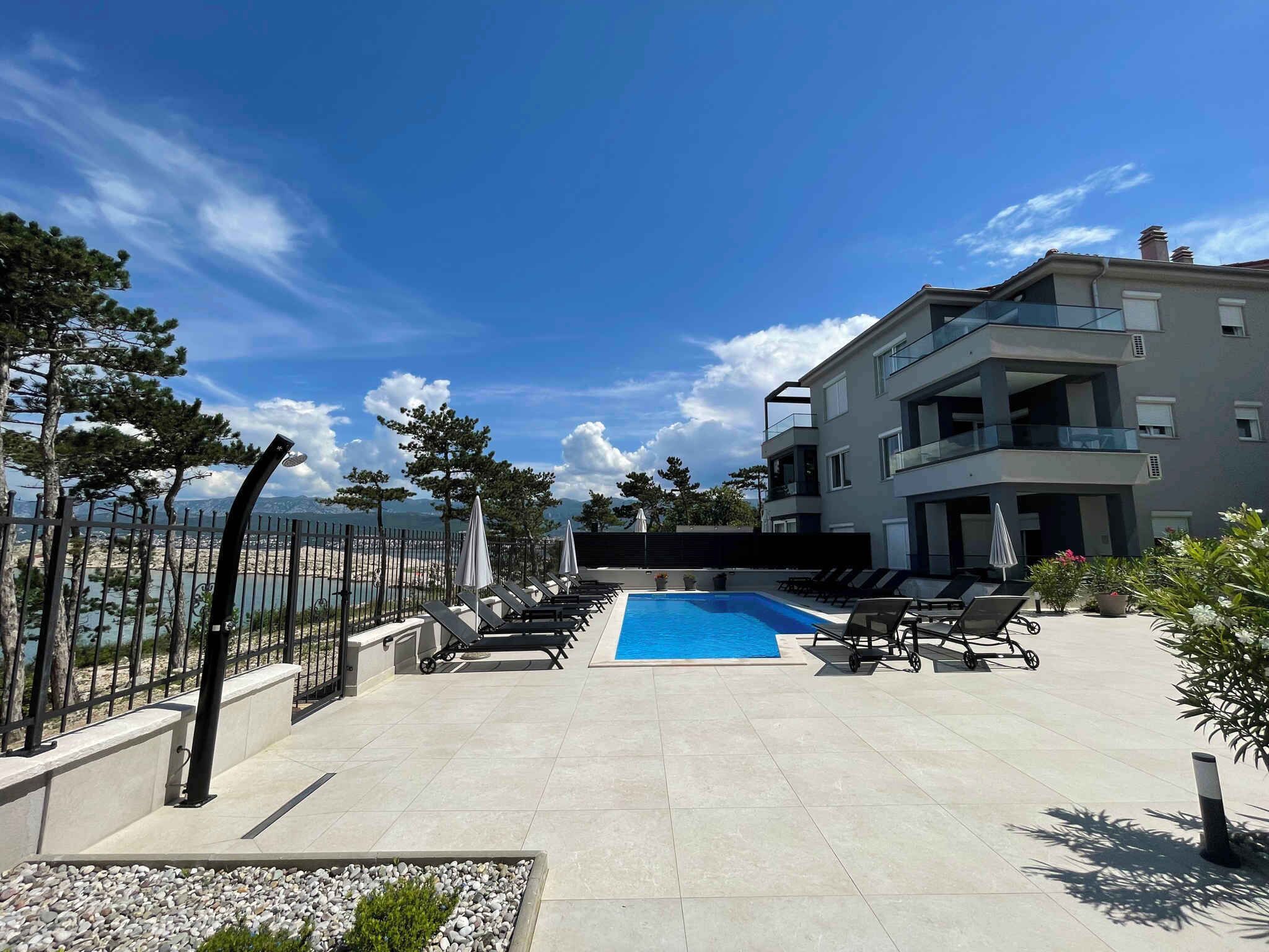 A modern outdoor pool area with lounge chairs and a view of the sea.