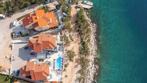 Vista aérea de una propiedad costera con varias edificaciones, piscina y un litoral rocoso.