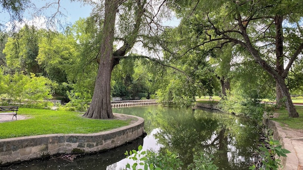 A serene park with a calm water body, lush greenery, and a stone pathway. - 5 mns to Sea World! Beautiful, updated 1story home with large backyard & playset (San Antonio)