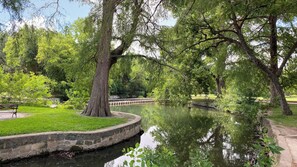 A serene park with a calm water body, lush greenery, and a stone pathway.