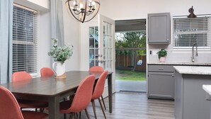 A modern kitchen with a dining area, featuring a wooden table, red chairs, a chandelier, and a view of the backyard. - 5 mns to Sea World! Beautiful, updated 1story home with large backyard & playset (San Antonio)