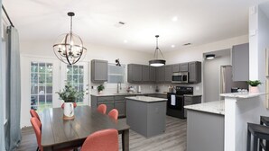 A modern kitchen with grey cabinets, a central island, and a dining area with a wooden table and red chairs. - 5 mns to Sea World! Beautiful, updated 1story home with large backyard & playset (San Antonio)