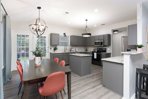 A modern kitchen with grey cabinets, a central island, and a dining area with a wooden table and red chairs.