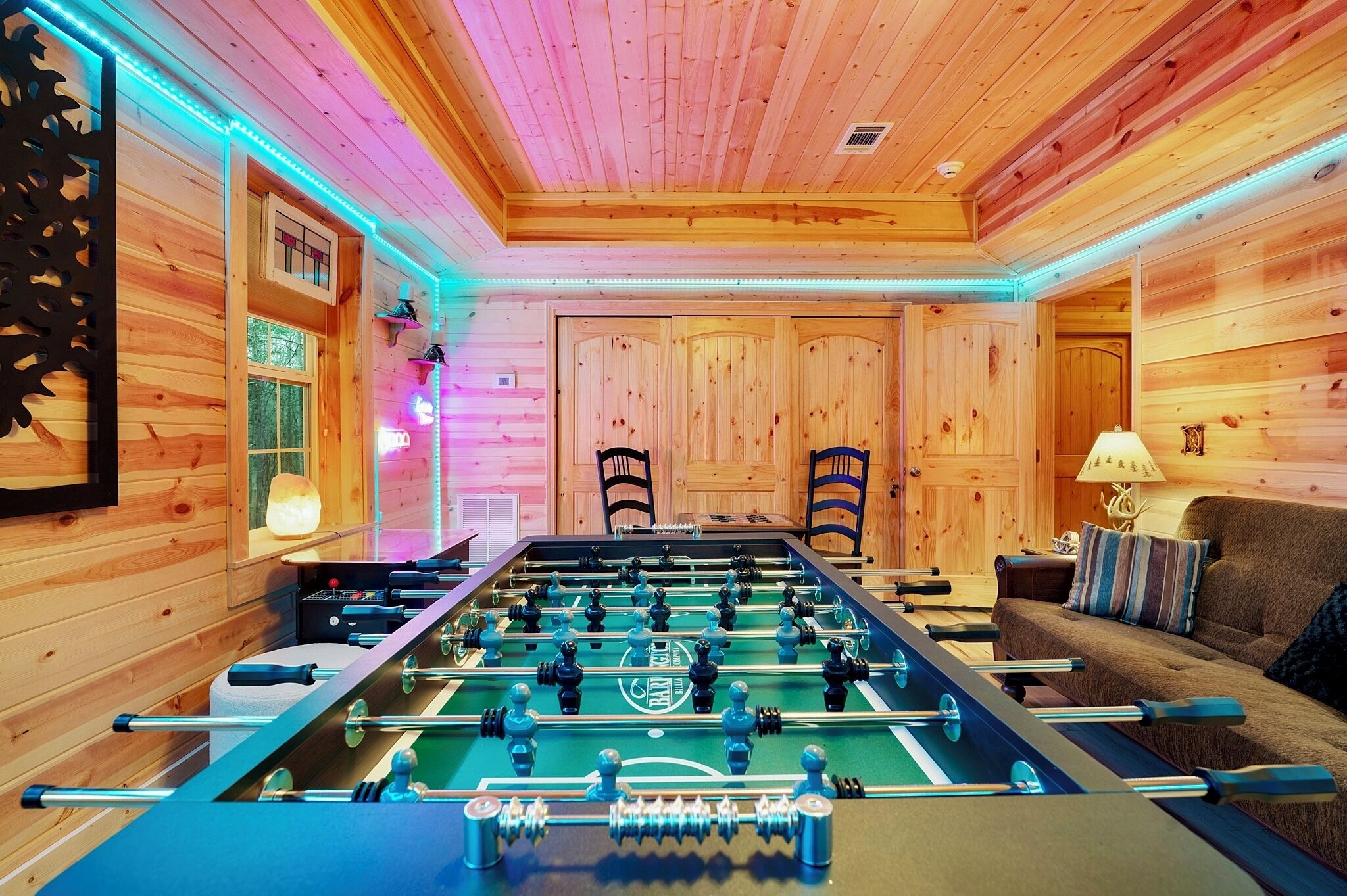 A room with a foosball table, wooden walls, and a sofa.