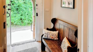 A wooden bench with floral cushions, a framed picture on the wall, and a doorway leading to a green outdoor area. - 2 bedroom accommodation in Wenhaston, near Halesworth (Wenhaston, near Halesworth)
