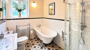 A bathroom with a white bathtub, a toilet, and a shower area with a glass door. - 2 bedroom accommodation in Wenhaston, near Halesworth (Wenhaston, near Halesworth)