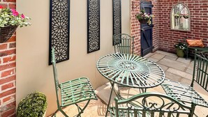 A patio with a round metal table and chairs, a brick wall, and decorative metal panels. - 2 bedroom accommodation in Wenhaston, near Halesworth (Wenhaston, near Halesworth)