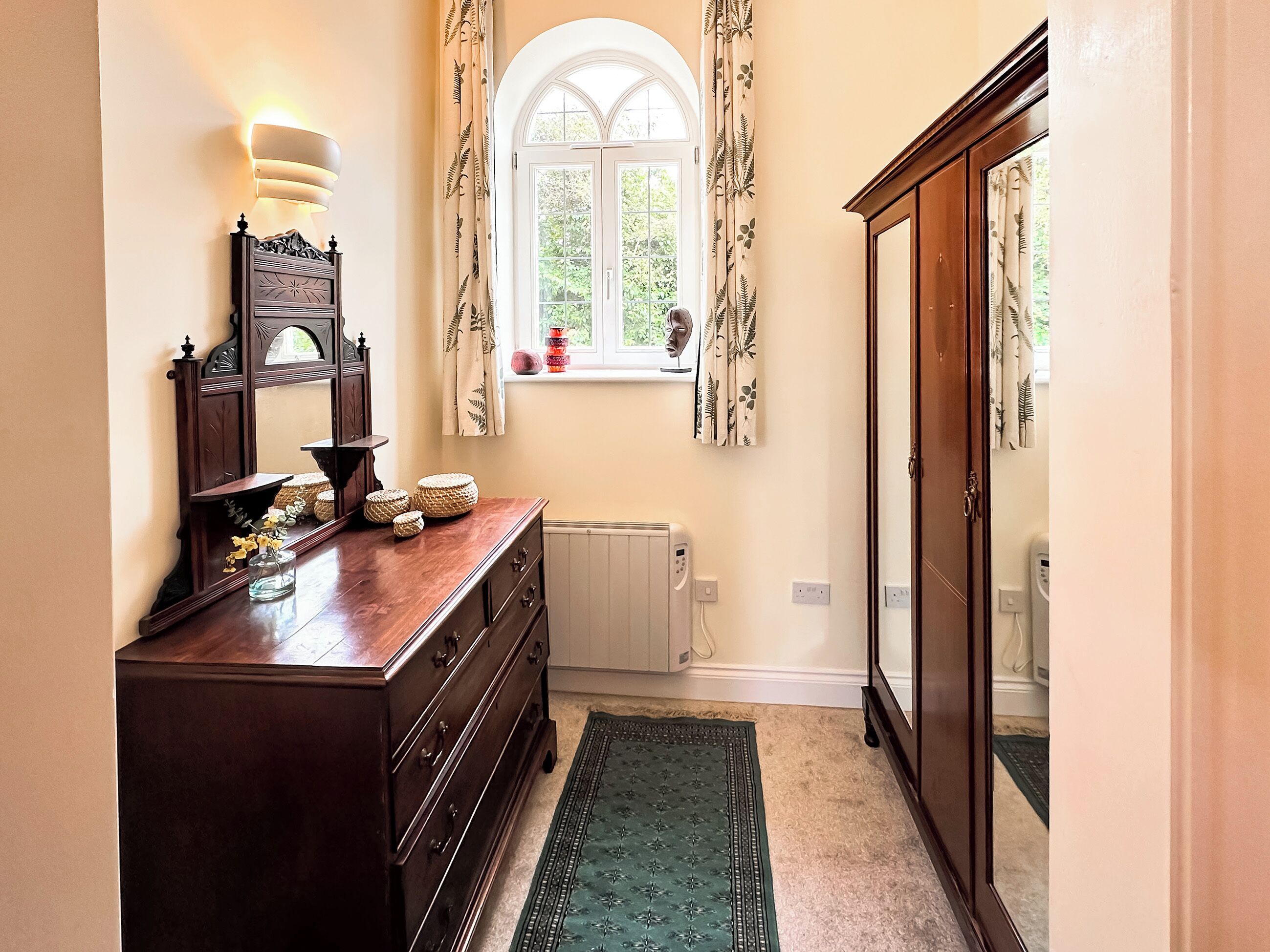 A hallway with a wooden dresser, a radiator, a window with curtains, and a mirror.
