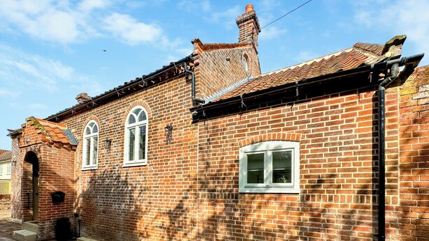 A brick building with two arched windows and a small door, a chimney, and a visible gutter system. - 2 bedroom accommodation in Wenhaston, near Halesworth (Wenhaston, near Halesworth)