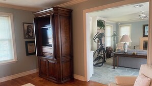 A living room with a dark wooden entertainment center, a beige sofa, and a patterned rug. - Private Coastal Home w/ Pool & Hot Tub • Enclosed Garden • Near Beaches (Corpus Christi)