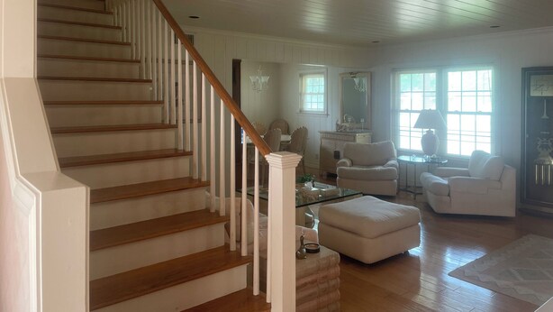 A spacious living room with a wooden staircase, white walls, and a large window providing natural light. - Private Coastal Home w/ Pool & Hot Tub • Enclosed Garden • Near Beaches (Corpus Christi)