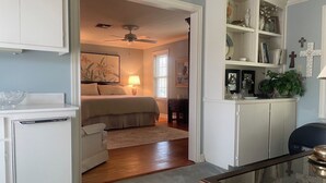 A bedroom with a bed, bedside table, lamp, and a view into another room. - Private Coastal Home w/ Pool & Hot Tub • Enclosed Garden • Near Beaches (Corpus Christi)