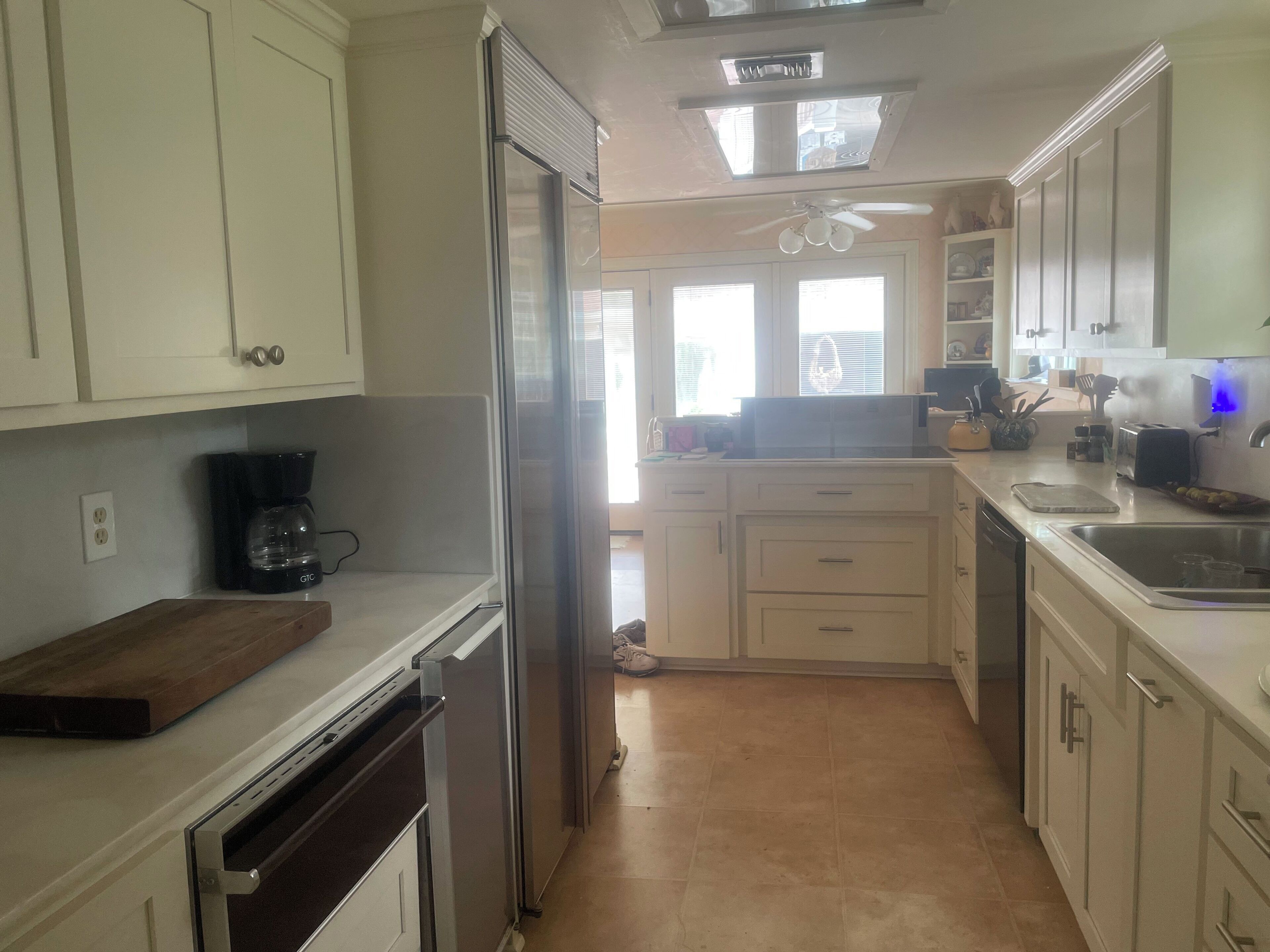 A kitchen with white cabinets, a stainless steel refrigerator, a coffee maker, and a ceiling fan.