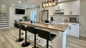 Una cocina moderna con una isla central, taburetes de bar, armarios blancos y un refrigerador de acero inoxidable.