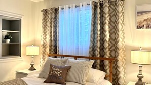 Una cama bien tendida con ropa de cama a rayas y una almohada con el texto 'hogar, dulce hogar', flanqueada por dos lámparas de noche.