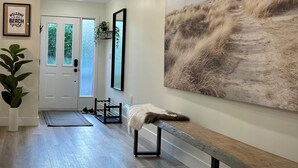 Un pasillo moderno con piso de madera, un banco, un cuadro abstracto grande y un letrero de bienvenida.