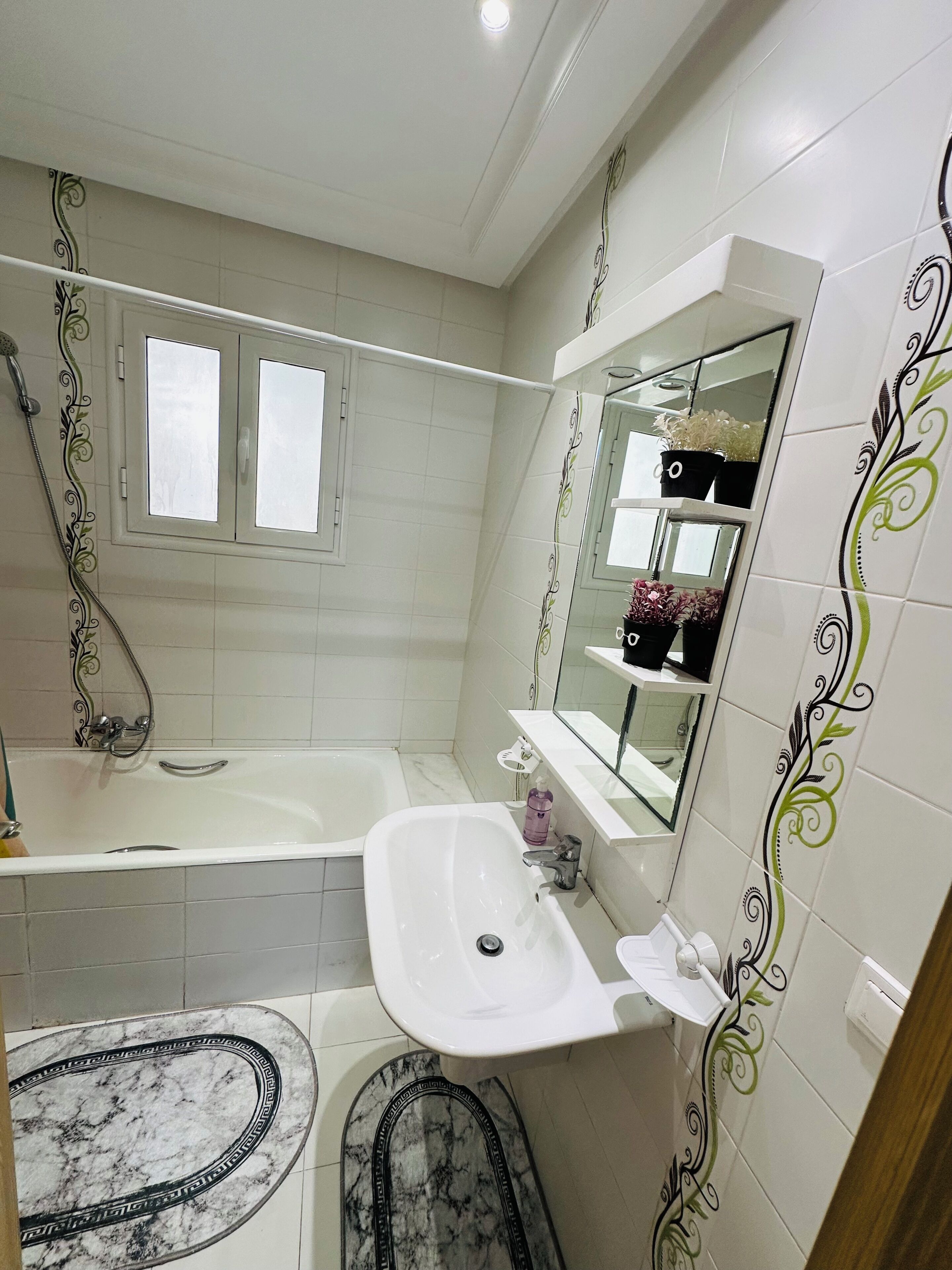 A bathroom with a bathtub, a sink, and a toilet. There is a window above the bathtub and a mirror above the sink.