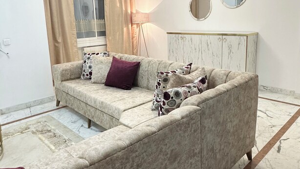 A living room with a beige sofa, a marble floor, a modern light fixture, and a large mirror on the wall. - Stunning 3 Bedroom Apartment in Khezema, Sousse Just 5 Minutes From the Beach! (Sousse)