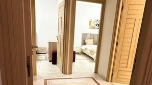 A hotel room with a large bed, a desk, and a chair. There is a wooden door and a window. - Stunning 3 Bedroom Apartment in Khezema, Sousse Just 5 Minutes From the Beach! (Sousse)