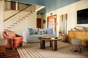 Uma sala de estar com escada, sofá, mesa de centro e um armário de madeira.