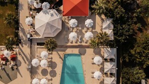 Vista aérea de uma área de piscina com vários guarda-sóis brancos, espreguiçadeiras e uma piscina central.