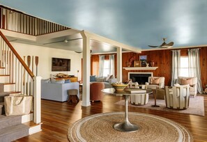 Uma sala de estar ampla, com lareira, escada e ventilador de teto.