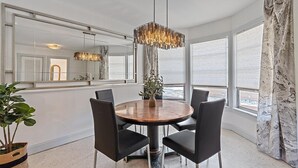 A modern dining area with a round wooden table, black chairs, a hanging light fixture, and large windows offering a view.