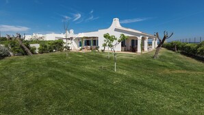 A white villa with a spacious lawn, a covered patio, and a view of the sea.