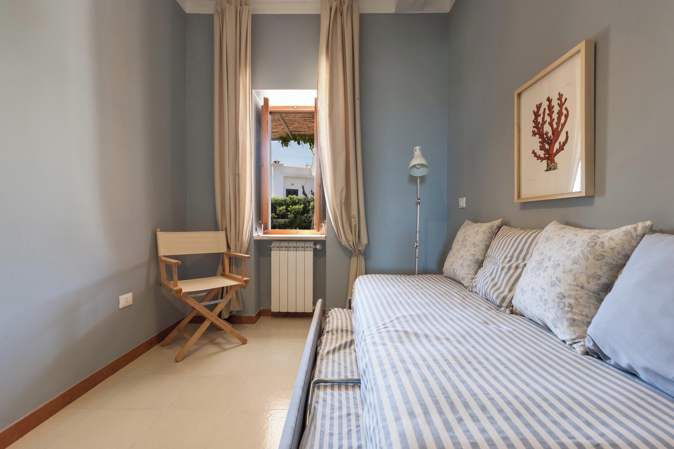 A bedroom with a bed, a chair, a radiator, and a window with curtains.